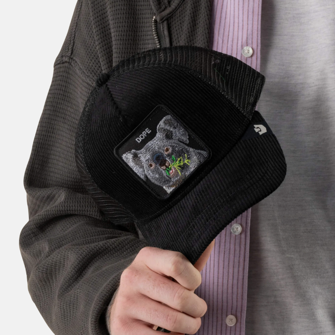 A person wearing a black corduroy cap with a square patch featuring a dog's face and the word 'DOGS'.