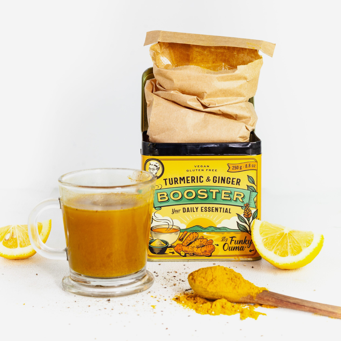 A jar of Turmeric & Ginger Booster powder with a kraft paper bag on top, styled with a glass mug of golden turmeric drink, a wooden spoon of yellow powder, and lemon slices on a white background.