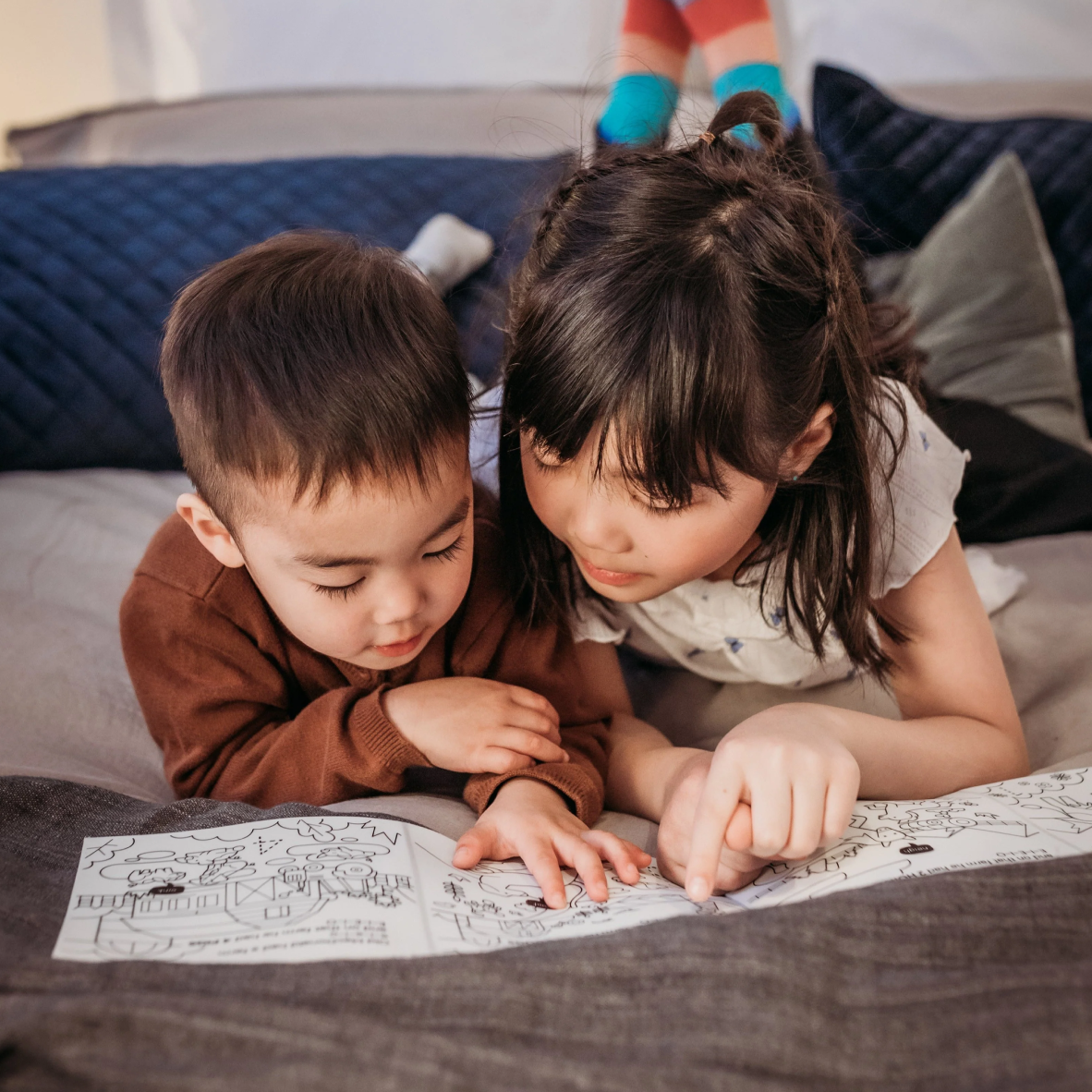 Two children looking at a coloring book on a bed.