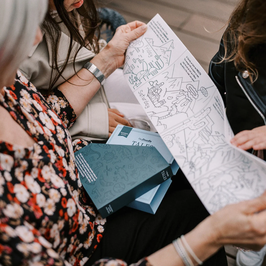 Two women looking at a coloring book with illustrations on a table.