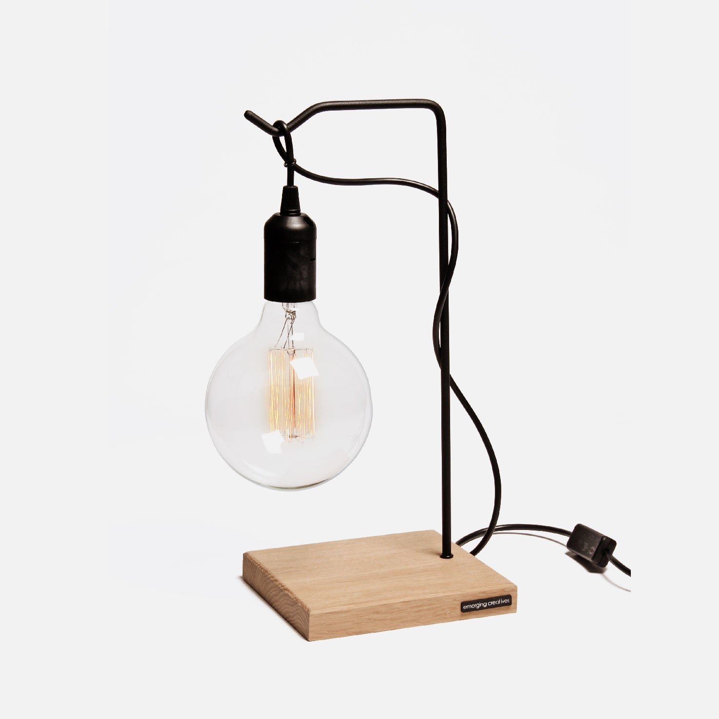 A stylish table lamp with a solid white oak base and a black powder-coated steel frame, featuring an Edison-style bulb, suspended by a black cord.